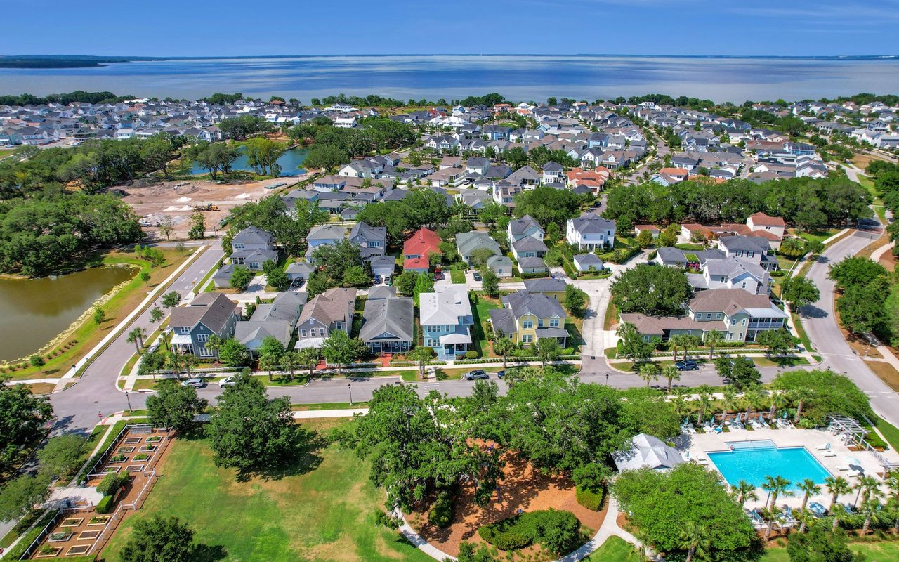 An aerial view of a residential neighborhood featuring various houses, a park, a pool, and scattered trees.