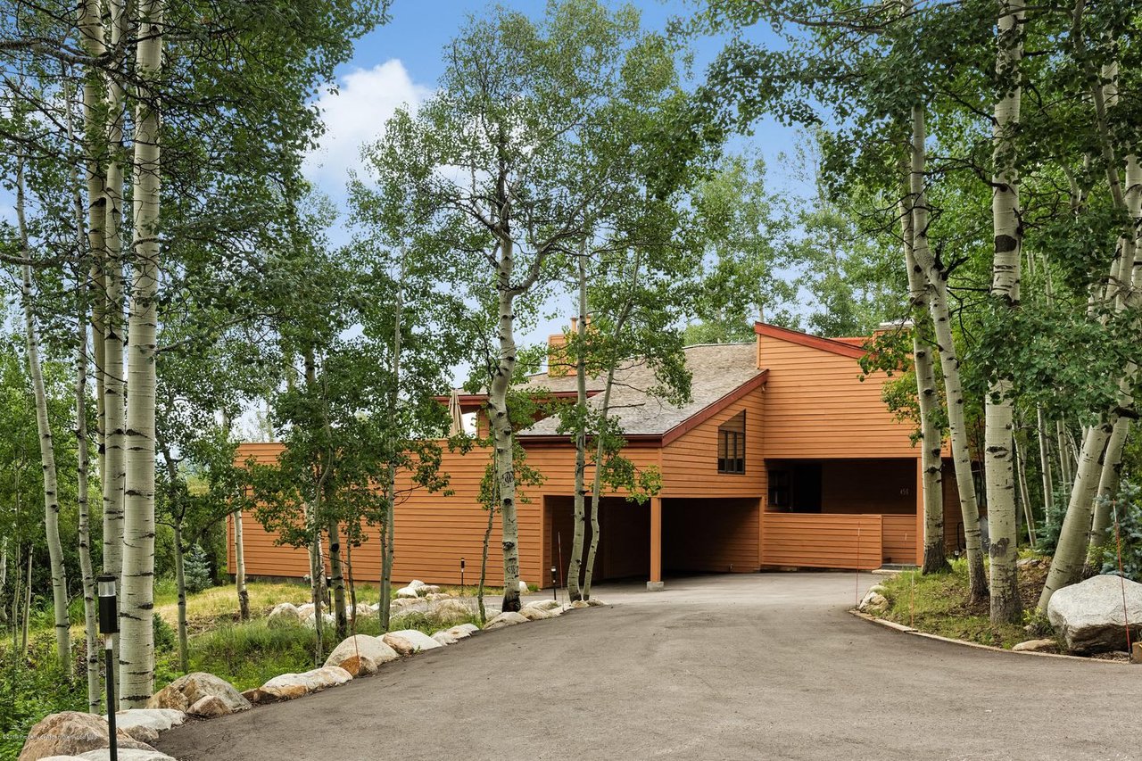 Orange-sided home among aspens, viewed from the driveway with covered parking.