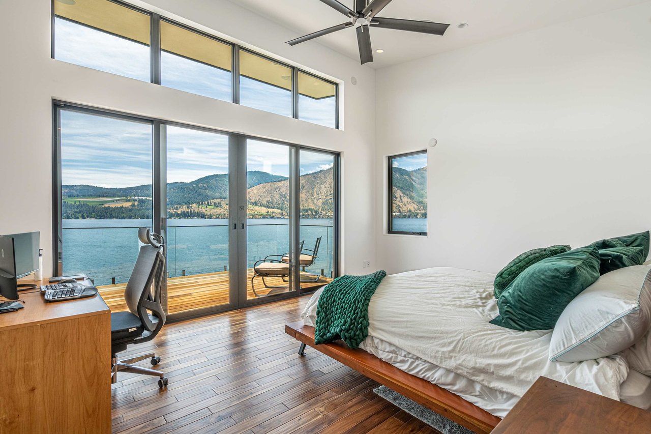  A modern bedroom with dark wood floors and white walls, featuring a bed with white and dark green bedding.