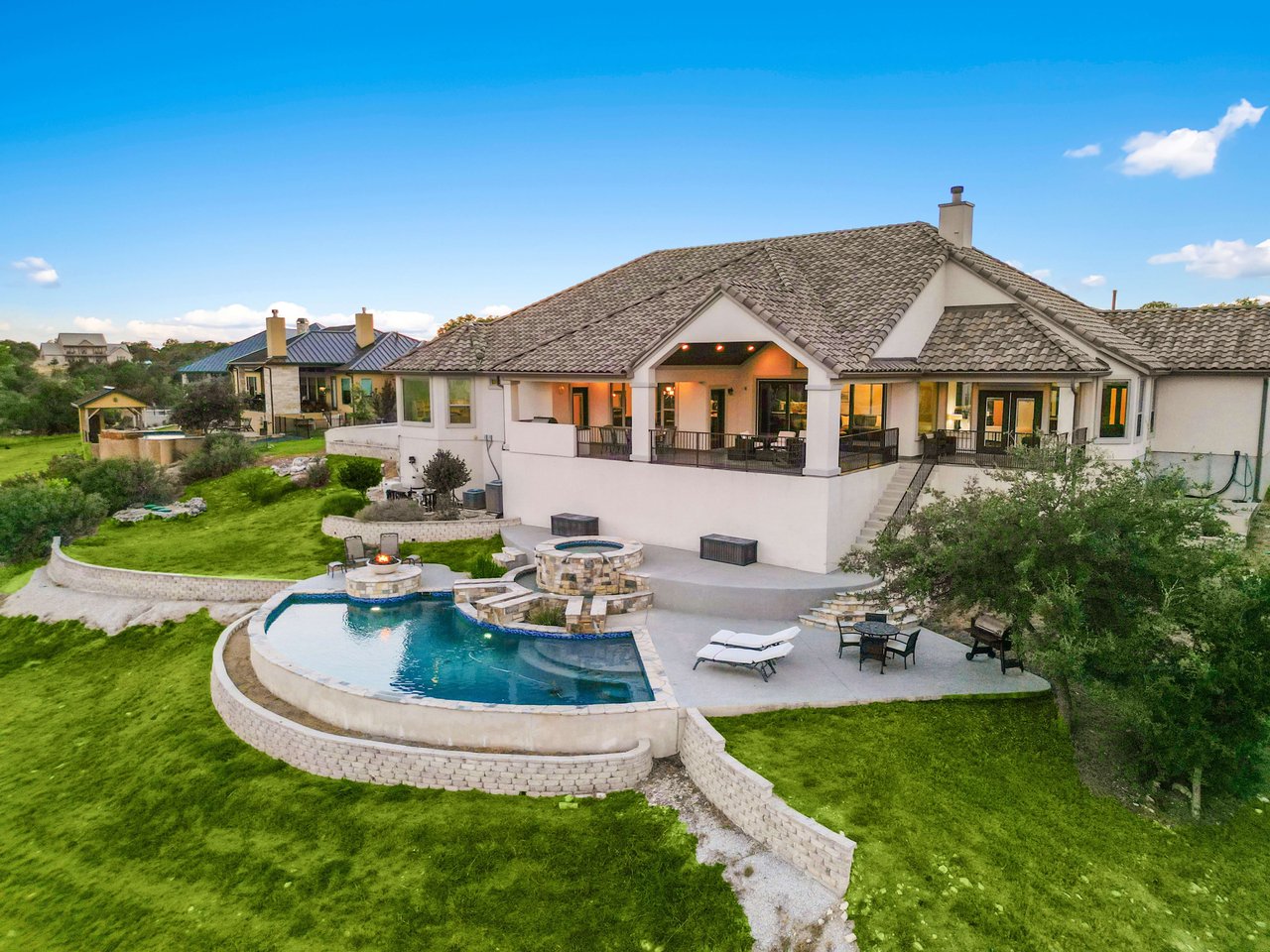 An aerial view of a luxurious house with a pool and a patio, set against a backdrop of rolling hills and a clear blue sky.