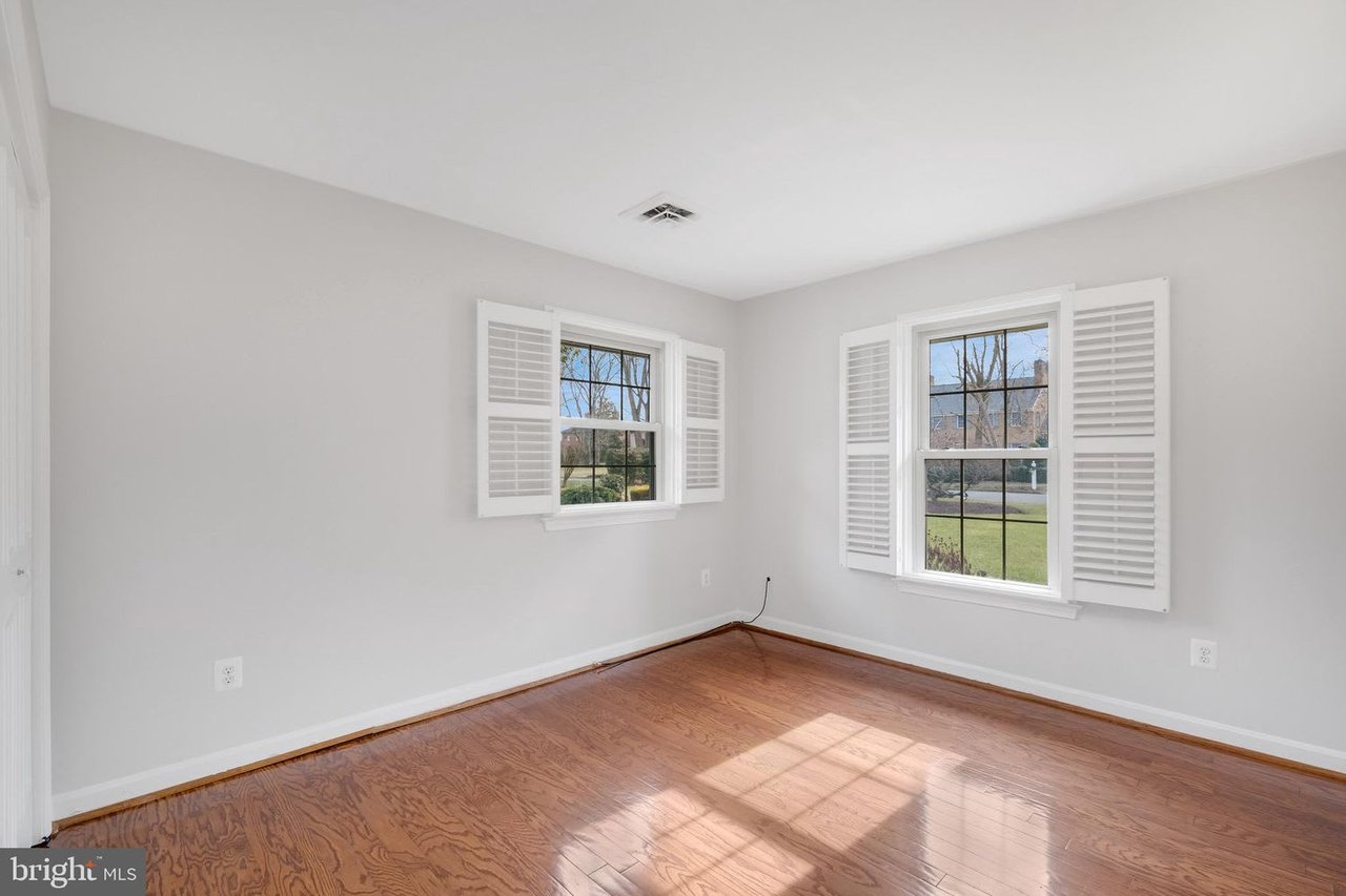 Empty room with hardwood floors and two shuttered windows lit by sunlight.