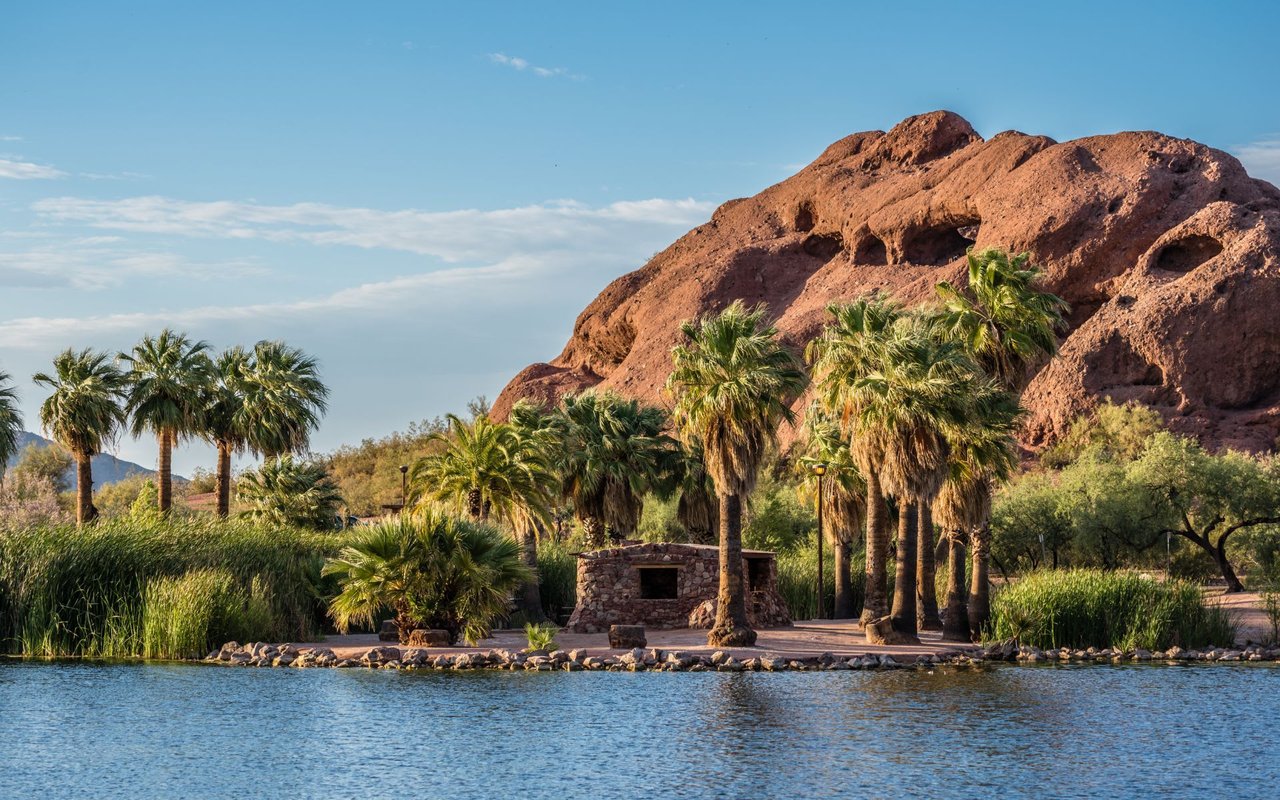 Tranquil desert retreat with palm trees, lake, and red rock, perfect for a peaceful escape near luxury homes.