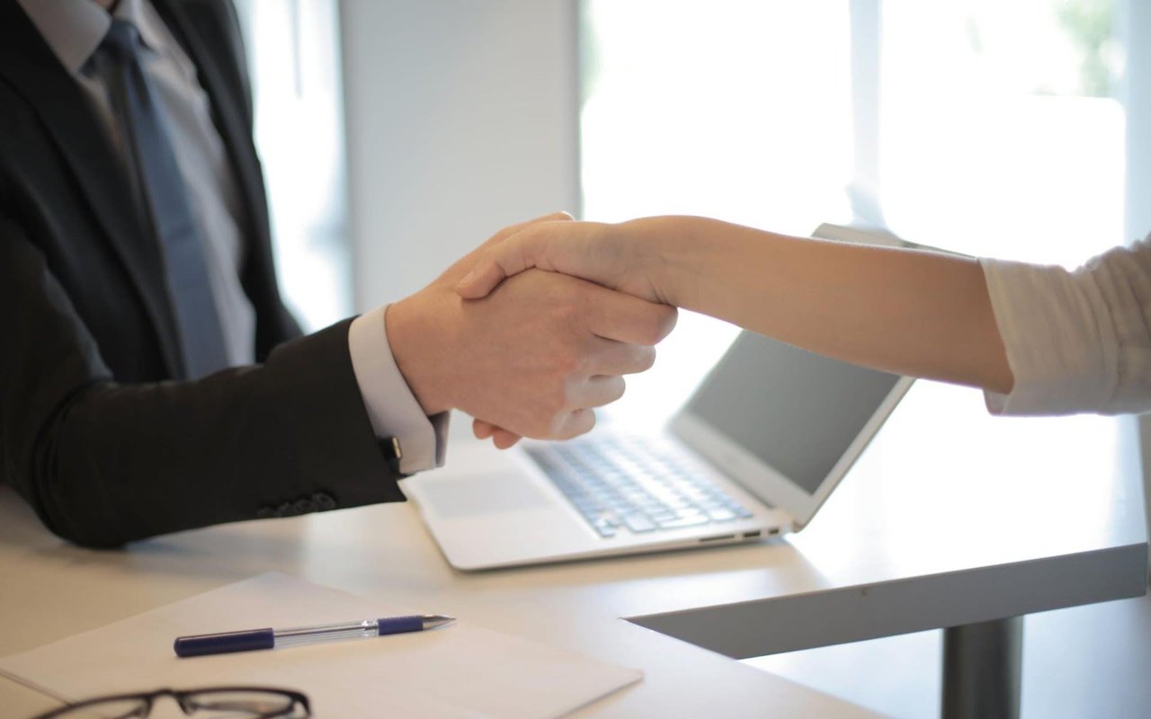 Two People Shaking Hands with a Pen and Laptop on the Table