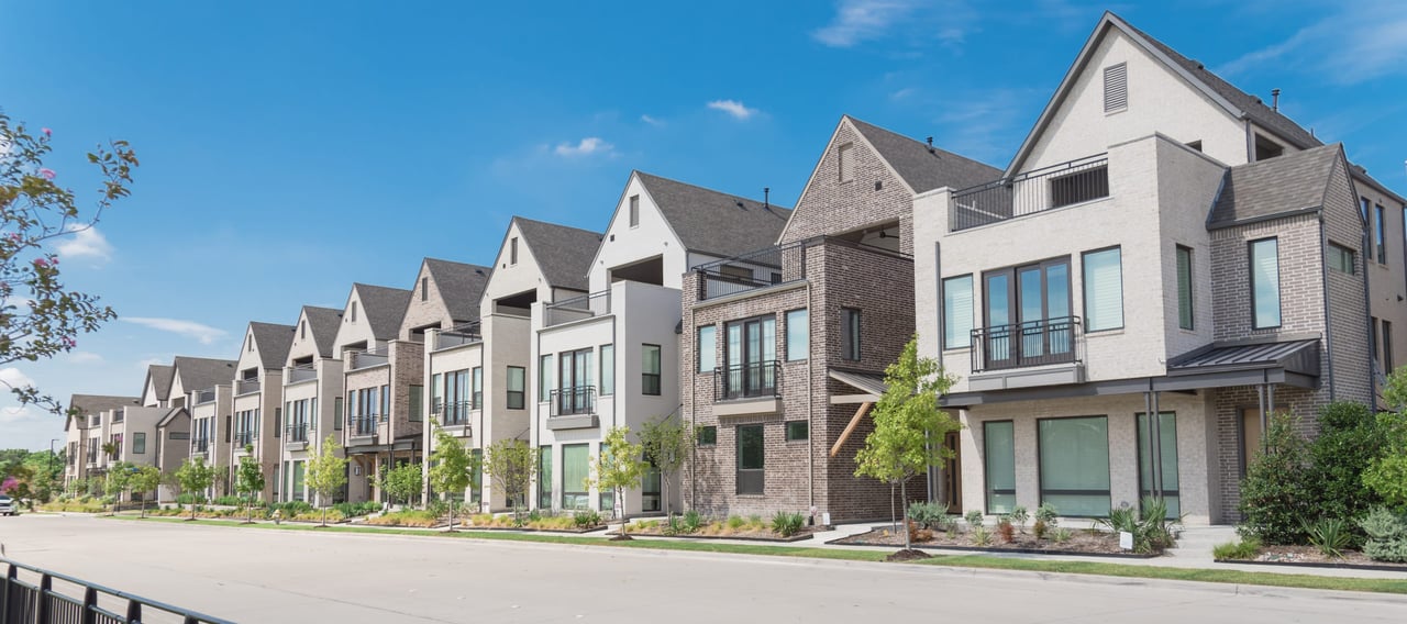 A row of houses with front porches and small front yards, all similar in design and color, in a residential neighborhood.