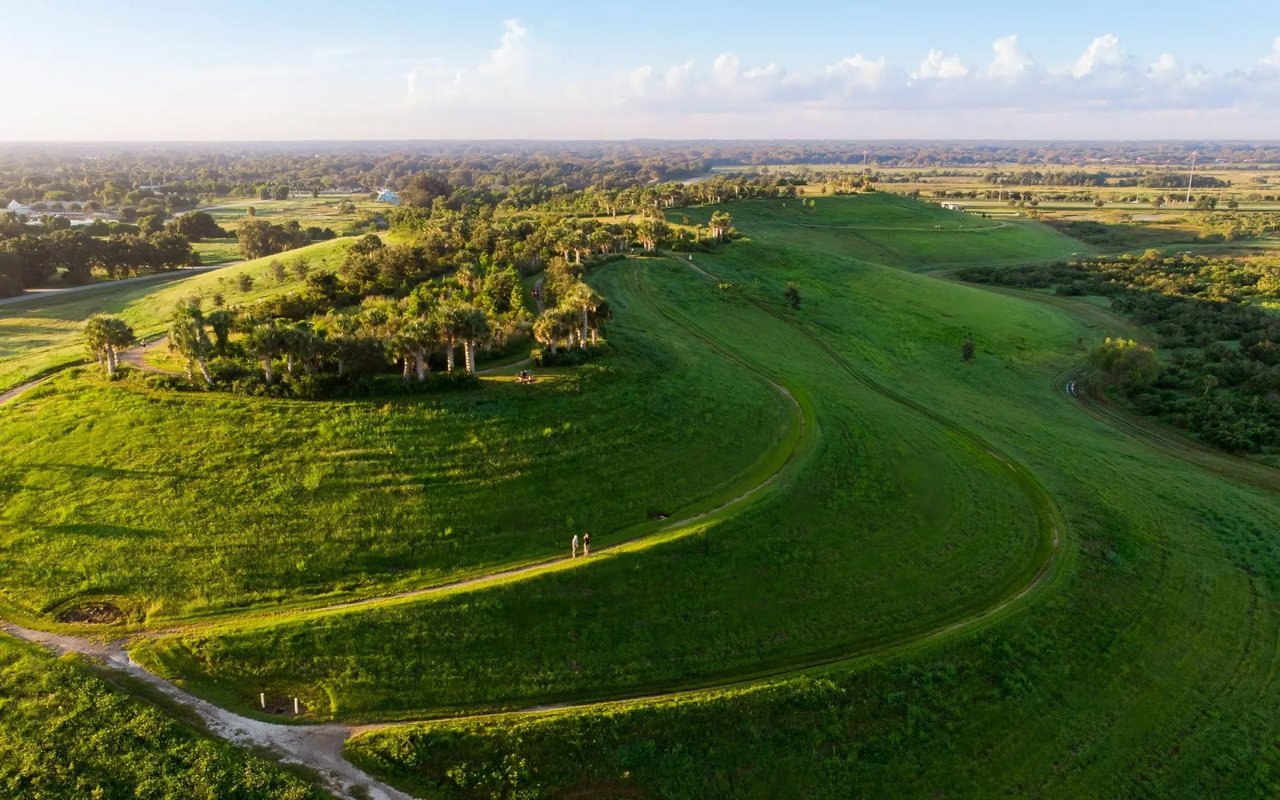 An aerial view shows vast, rolling green hills under a bright sky with scattered clouds.