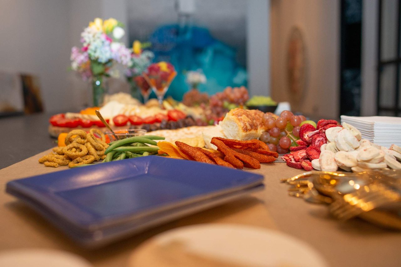 Buffet spread with antipasti, bread, grapes, dried fruit, and a blue plate in the foreground.