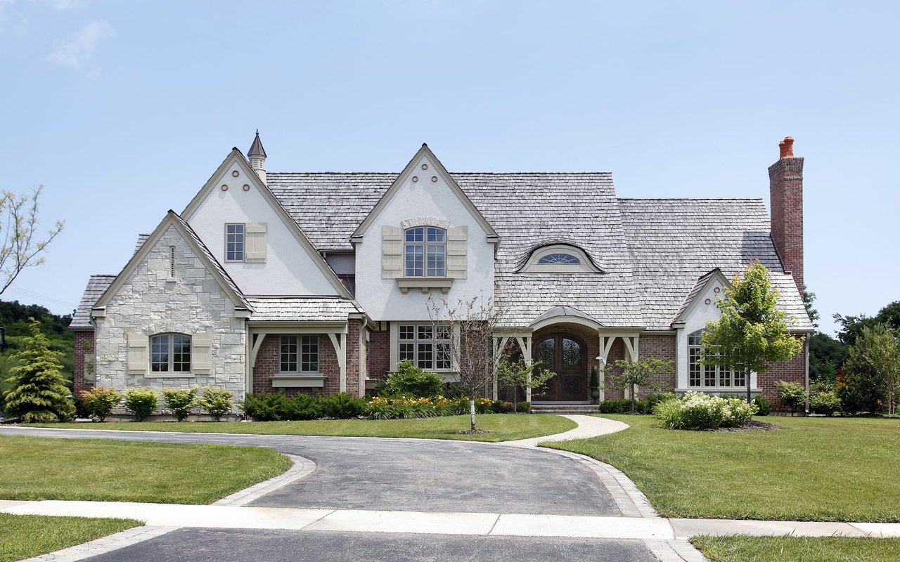 A large white house with a black asphalt driveway winding its way through a green lawn