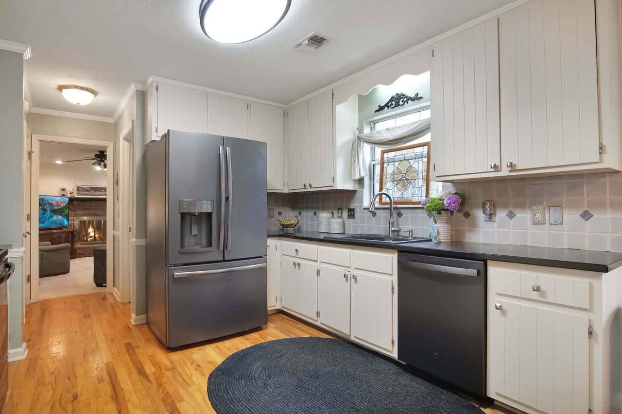 An interior shot of a kitchen with white cabinets, stainless steel appliances, and wooden flooring. The kitchen has a clean, modern design with plenty of natural light.