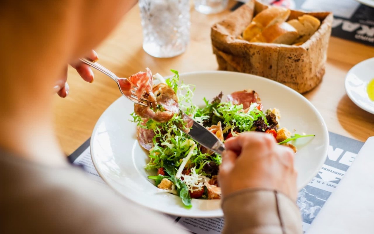 Image of Italian salad on a plate with fork and knife held by a woman