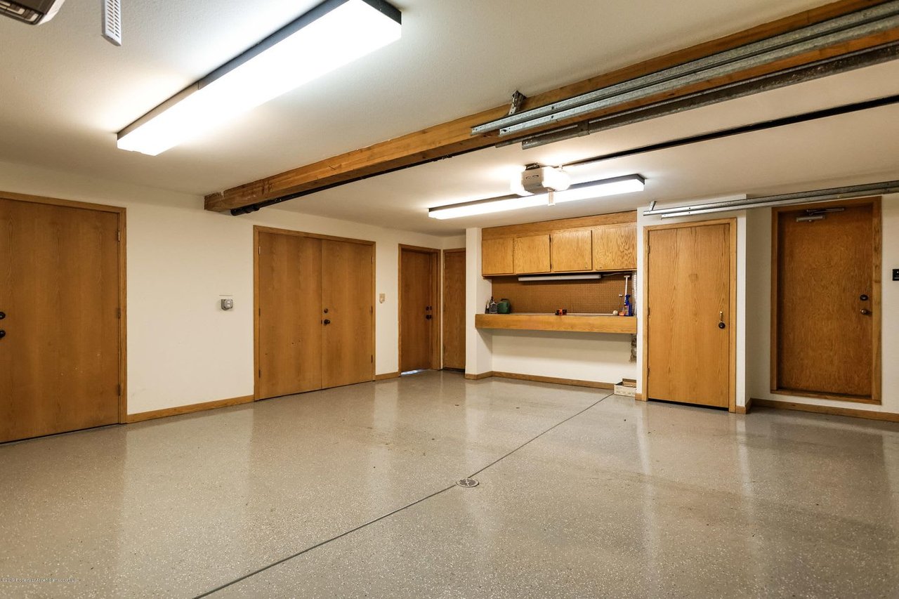 Vacant garage with a speckled floor, wooden doors, overhead tracks, and a built-in counter with cabinets.