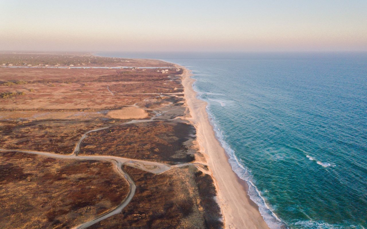 Ariel view of ocean, sandy beach, and bluffs at sunset in Polpis.