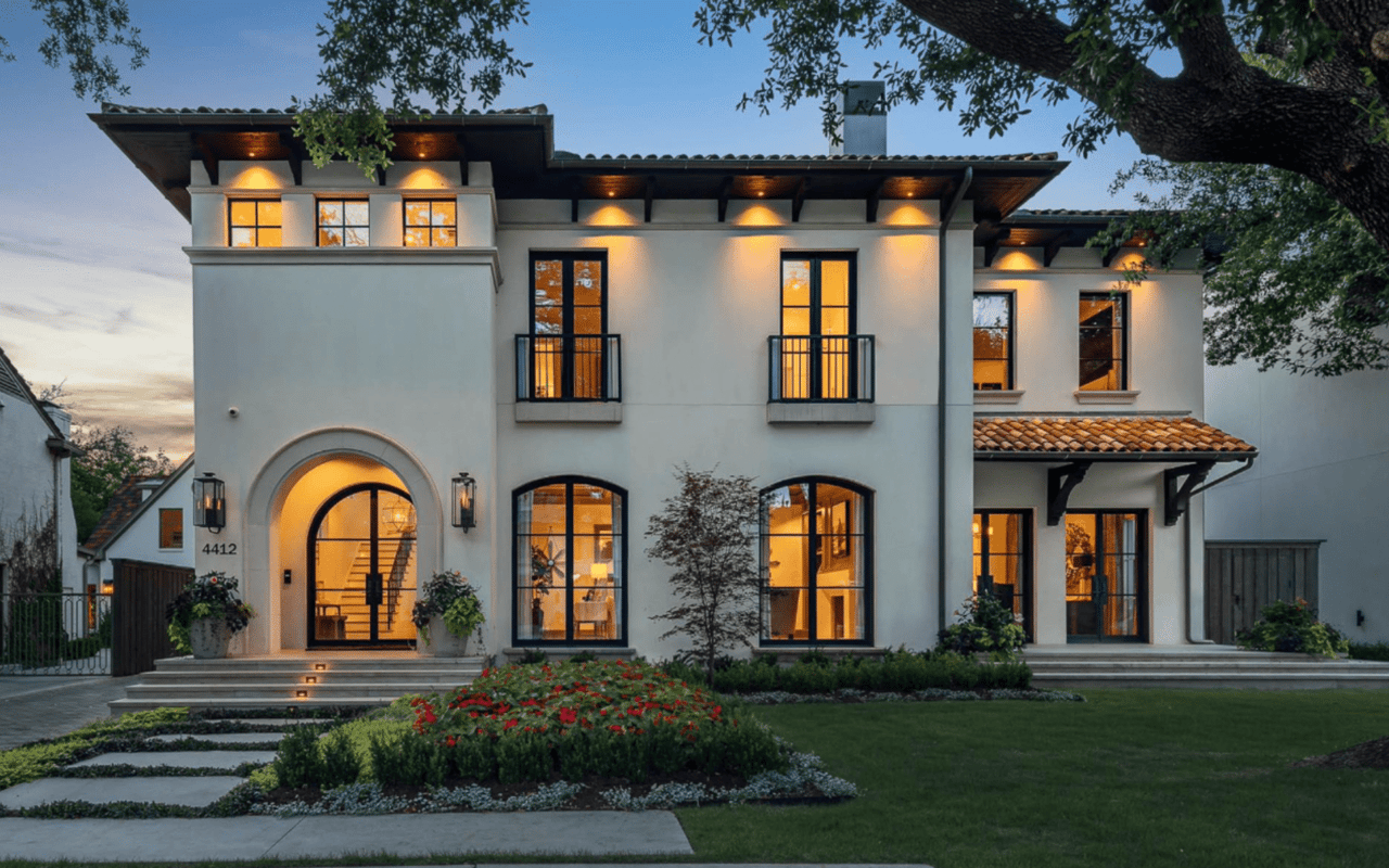 A grand Mediterranean Revival-style mansion with wrought iron balconies, large windows, a walkway, and a front lawn.