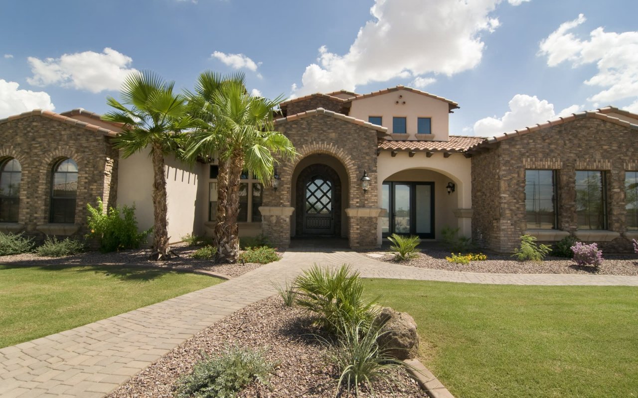 Mediterranean-style luxury home with stone exterior, arched entry, and palm trees.