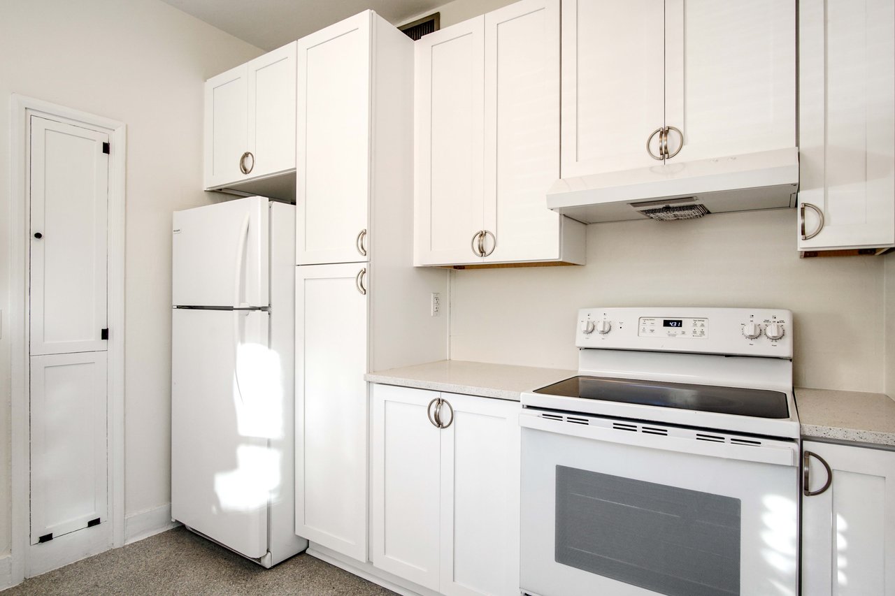 A view of the kitchen highlighting the refrigerator and stove. The kitchen is equipped with white cabinets and countertops.