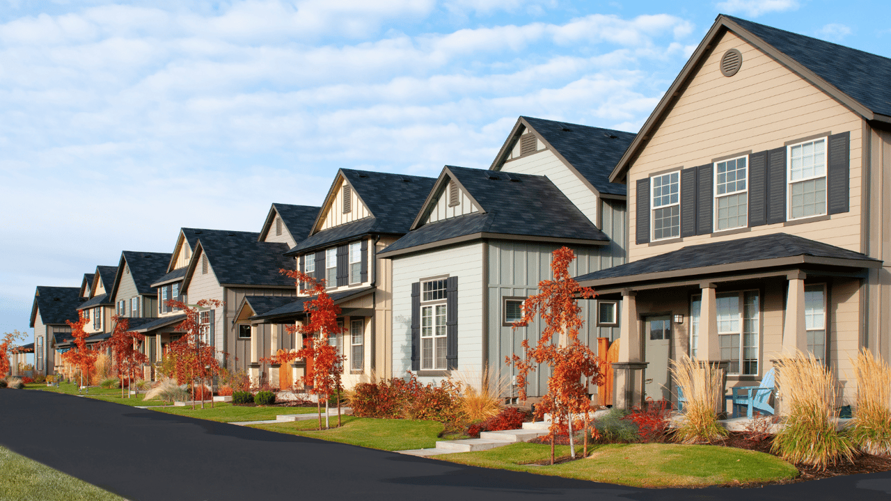 Row of suburban homes with covered porches, landscaped yards, and red autumn trees.