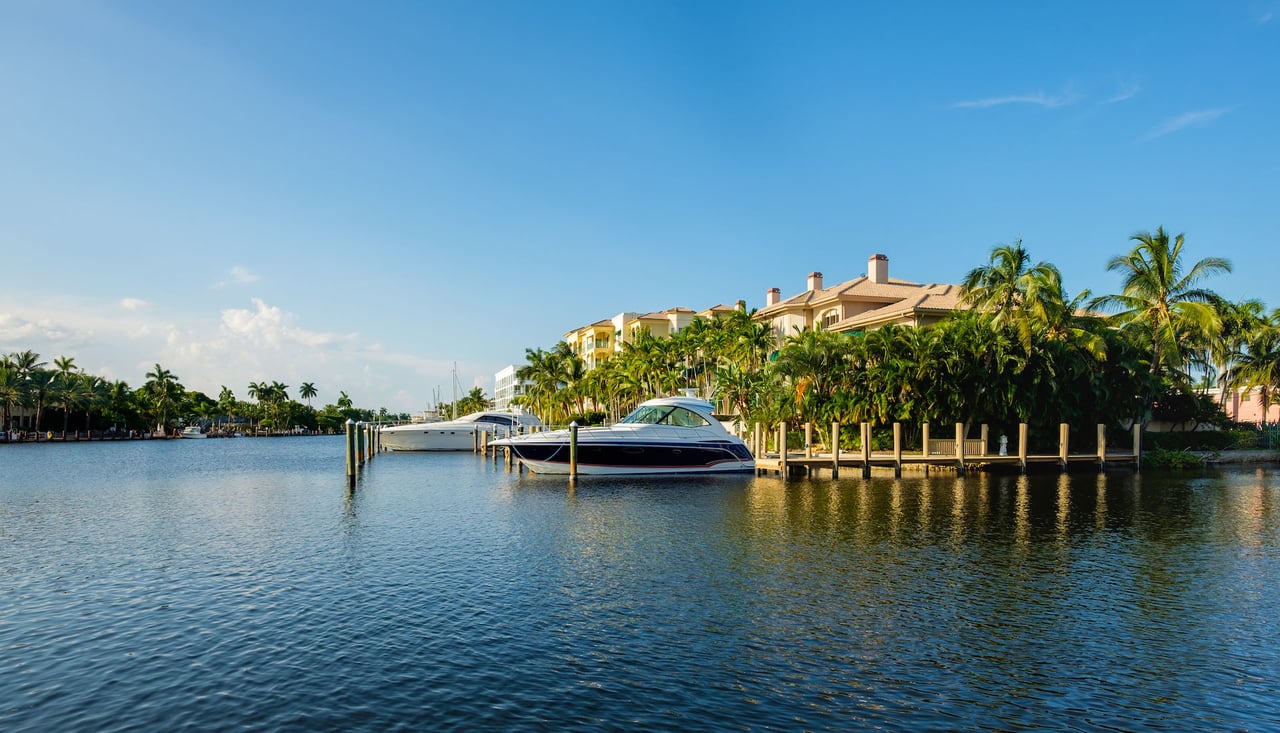 two boats docked in a canal in front of a house surrounded by palm trees