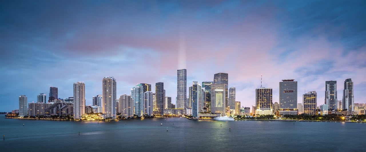 Waterfront skyline at dusk, with illuminated high-rises reflected across the water.