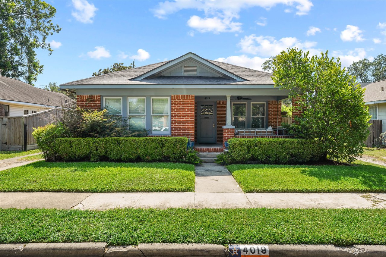 A single-family red brick house with a front lawn, a covered porch, a sidewalk, and a two-car garage attached on the left.