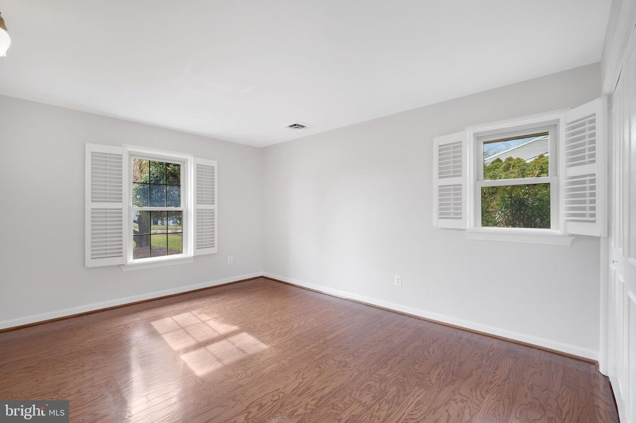 Empty room with hardwood floors and two windows with white plantation shutters.