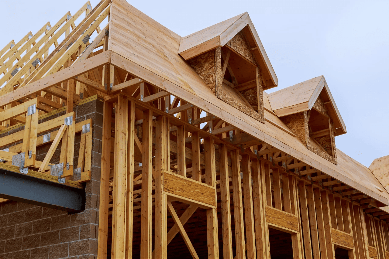 Home under construction with exposed timber framing and unfinished gabled roof sections.