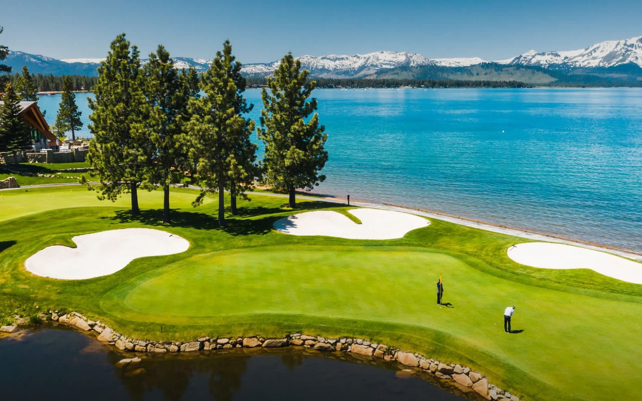 Stunning golf course overlooking a serene lake with snow-capped mountains in the background.