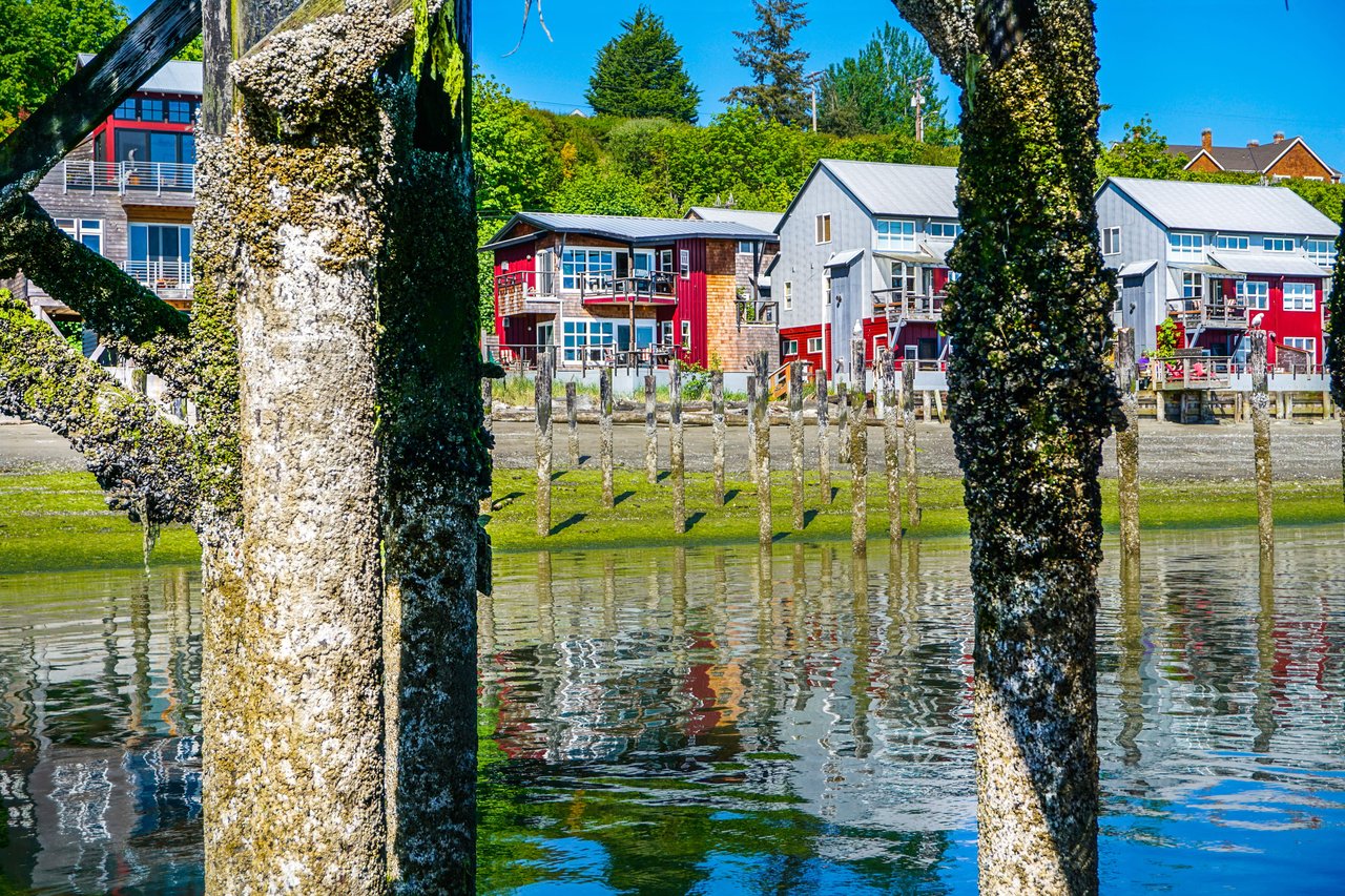 Wooden pier with reflections of houses in the water. The pier is long and narrow, and it extends out into a body of water. 