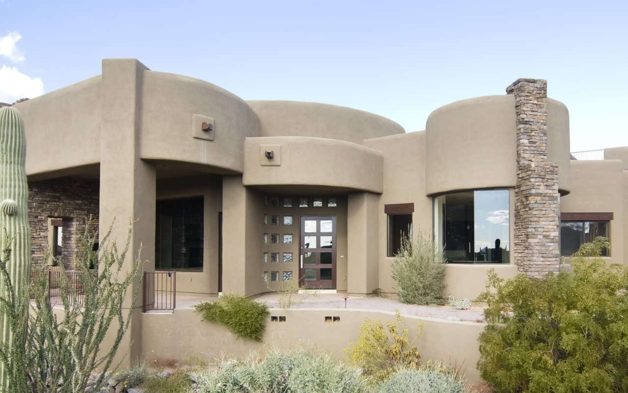 Modern desert oasis featuring a stucco home with curved lines, stone accents, and expansive windows.