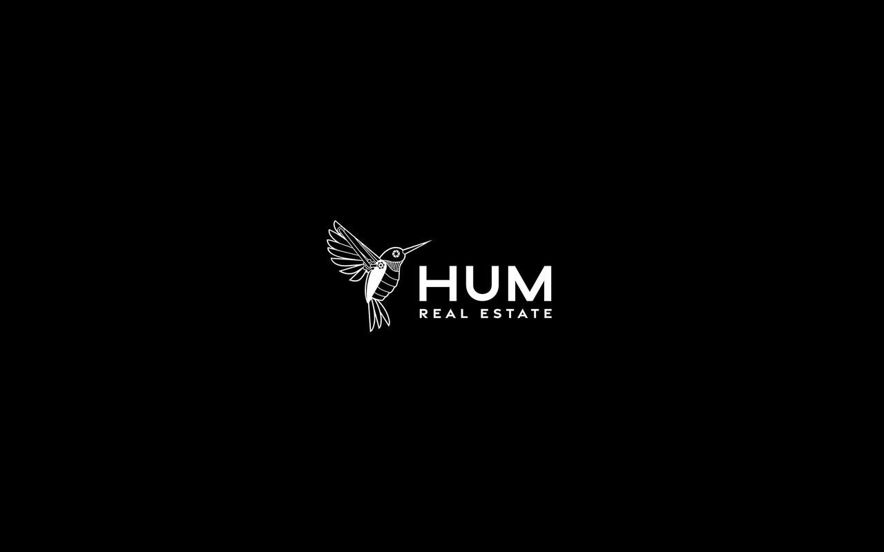 The HUM Real Estate logo featuring a stylized hummingbird, set against a black background. The logo is white.