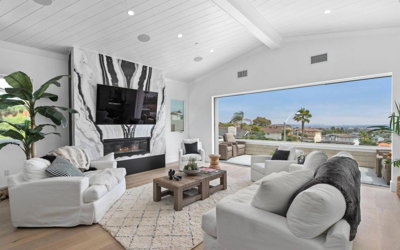  Two white slipcovered sofas with dark throw pillows are arranged around a rectangular wooden coffee table placed on a large, textured cream-colored rug.