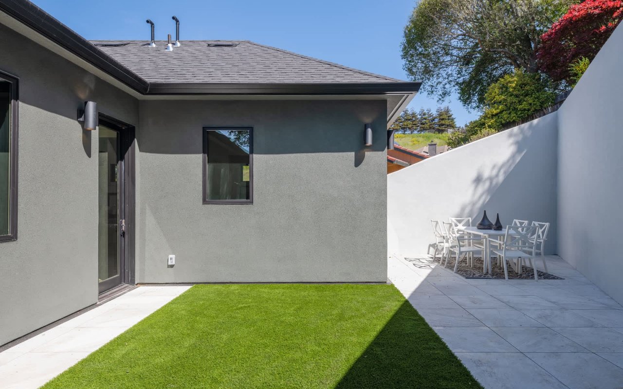 Modern gray home courtyard with a small lawn and white outdoor dining set.