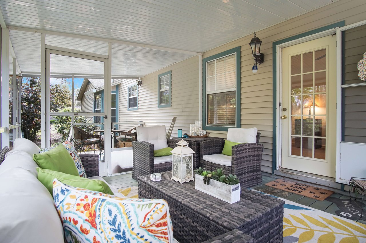 A screened porch or sunroom with wicker furniture and colorful cushions. The area is well-furnished and provides a comfortable space for relaxation.