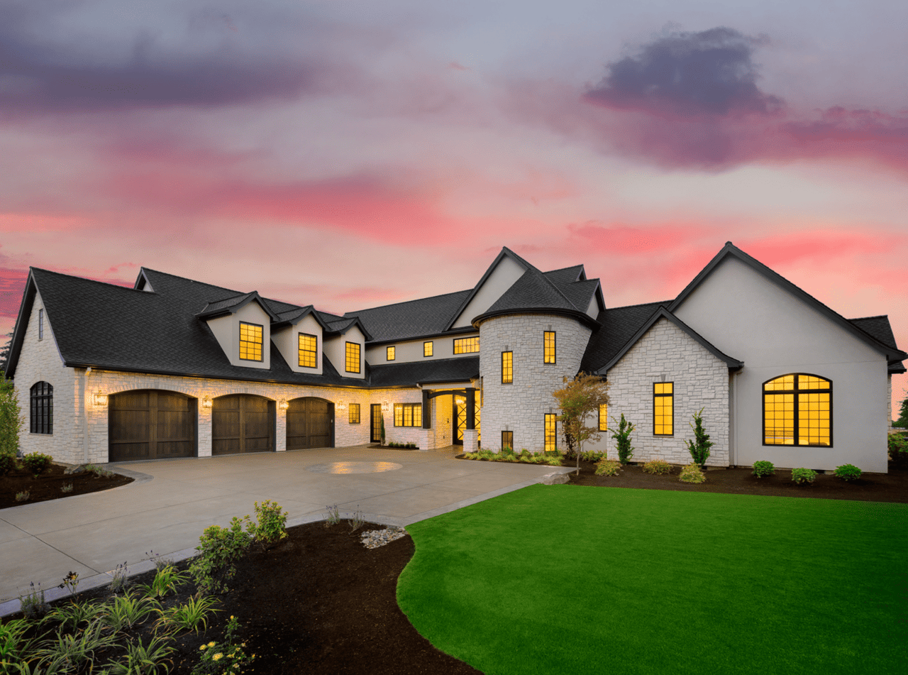 A large white house with a black roof sits on a green lawn at sunset.