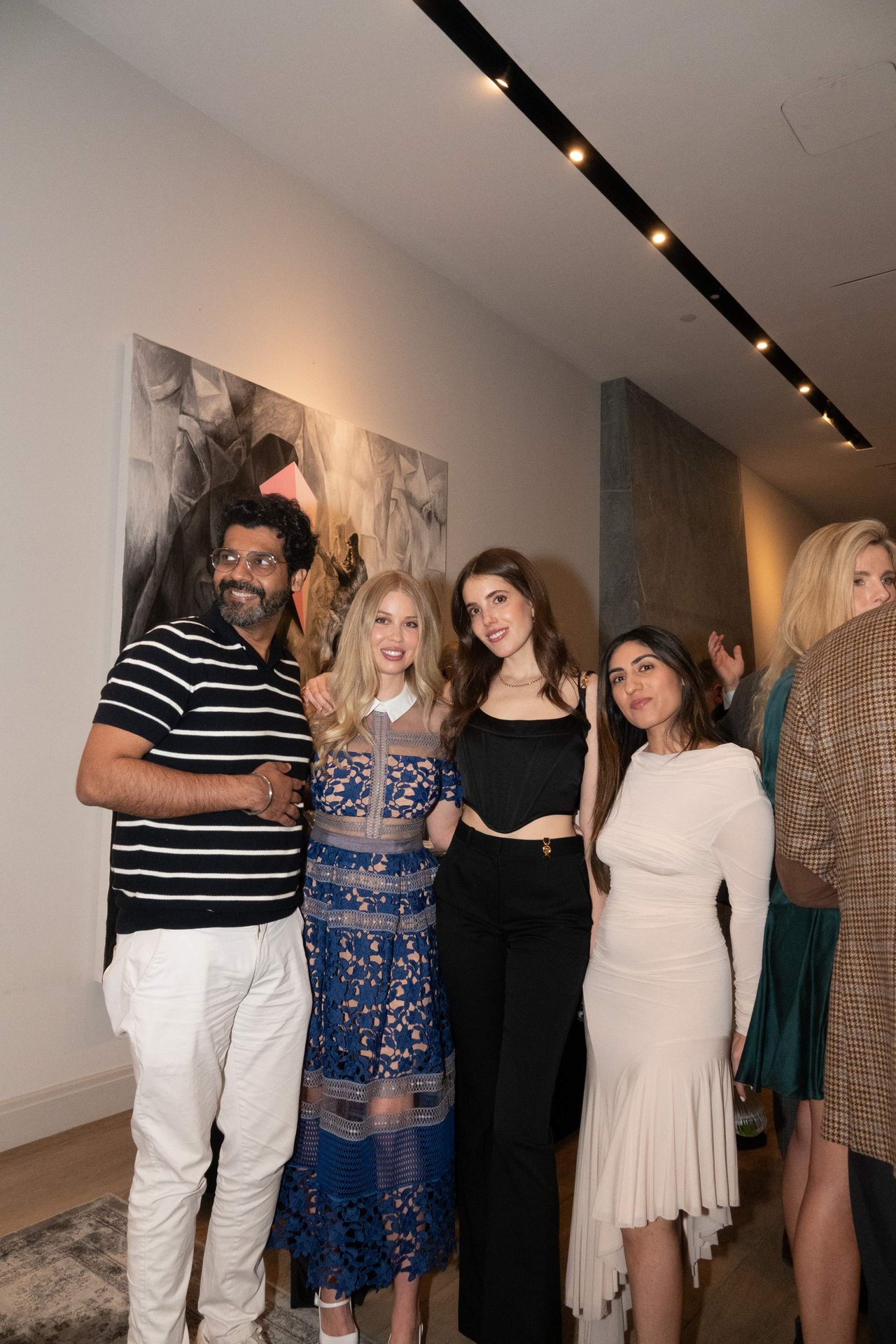 Seven people pose together indoors, with abstract wall art behind them.