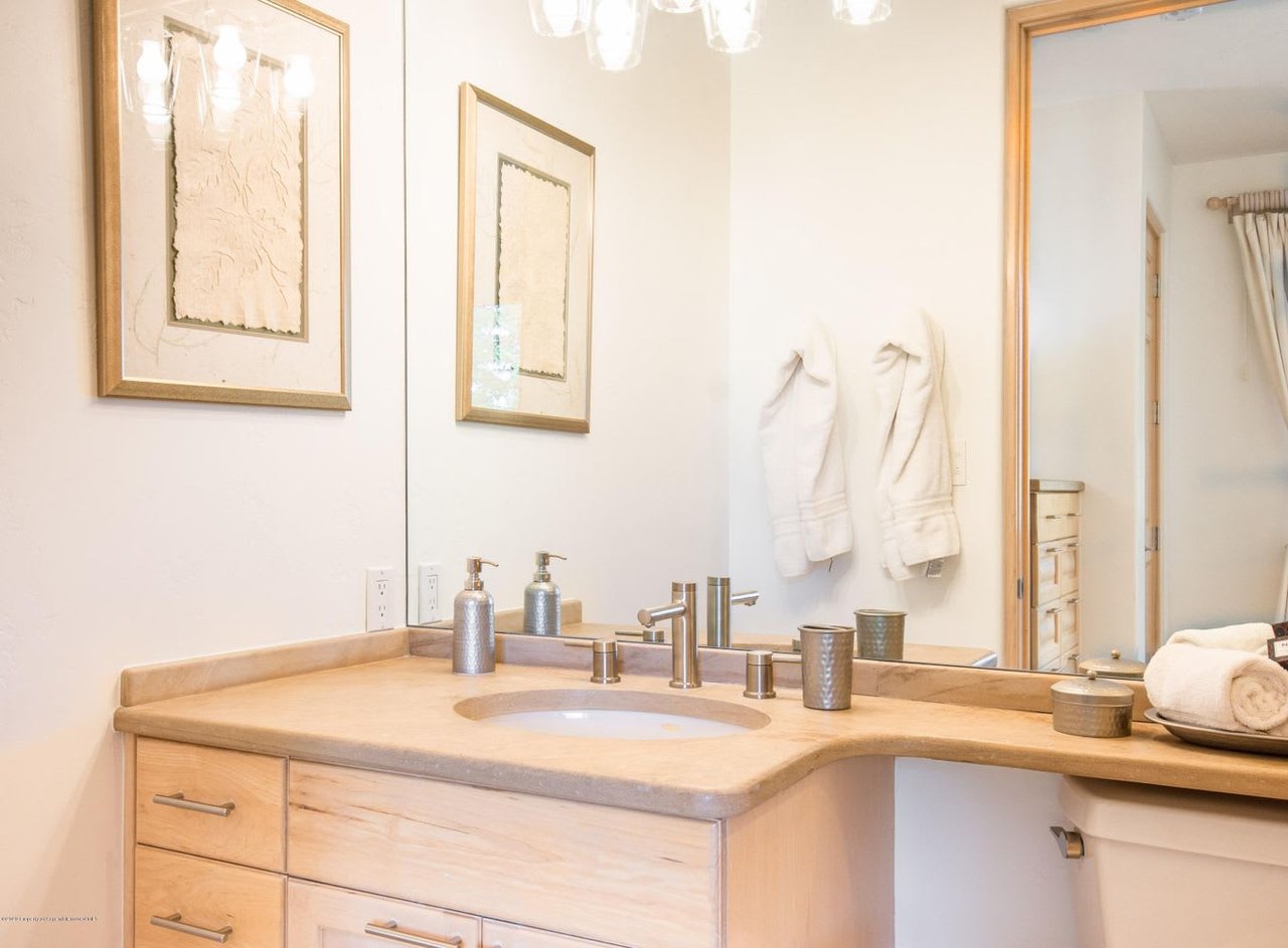 Bathroom vanity with a pale stone counter, inset sink, and light wood cabinetry.