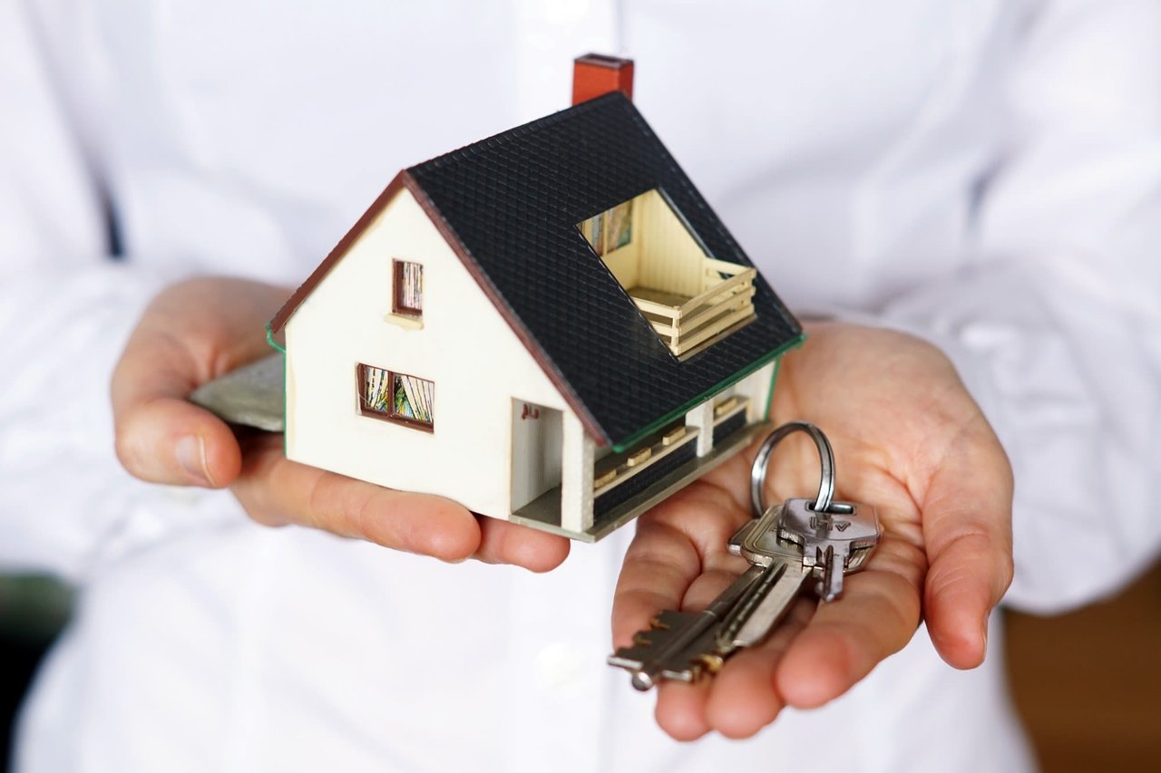 A model house and keys rest in open hands.