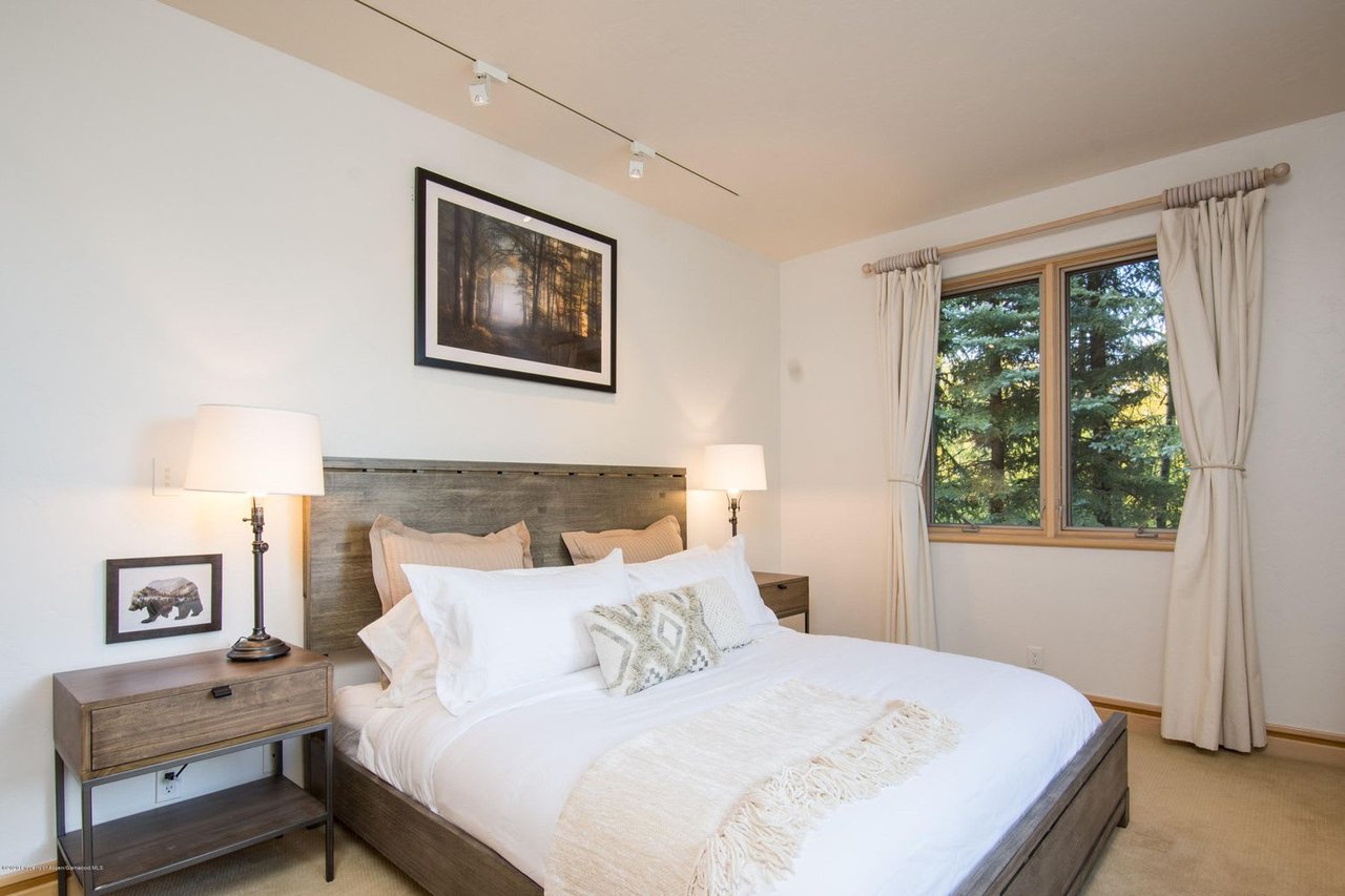 Bedroom with white bedding, rustic wood furniture, and a window overlooking evergreen trees.