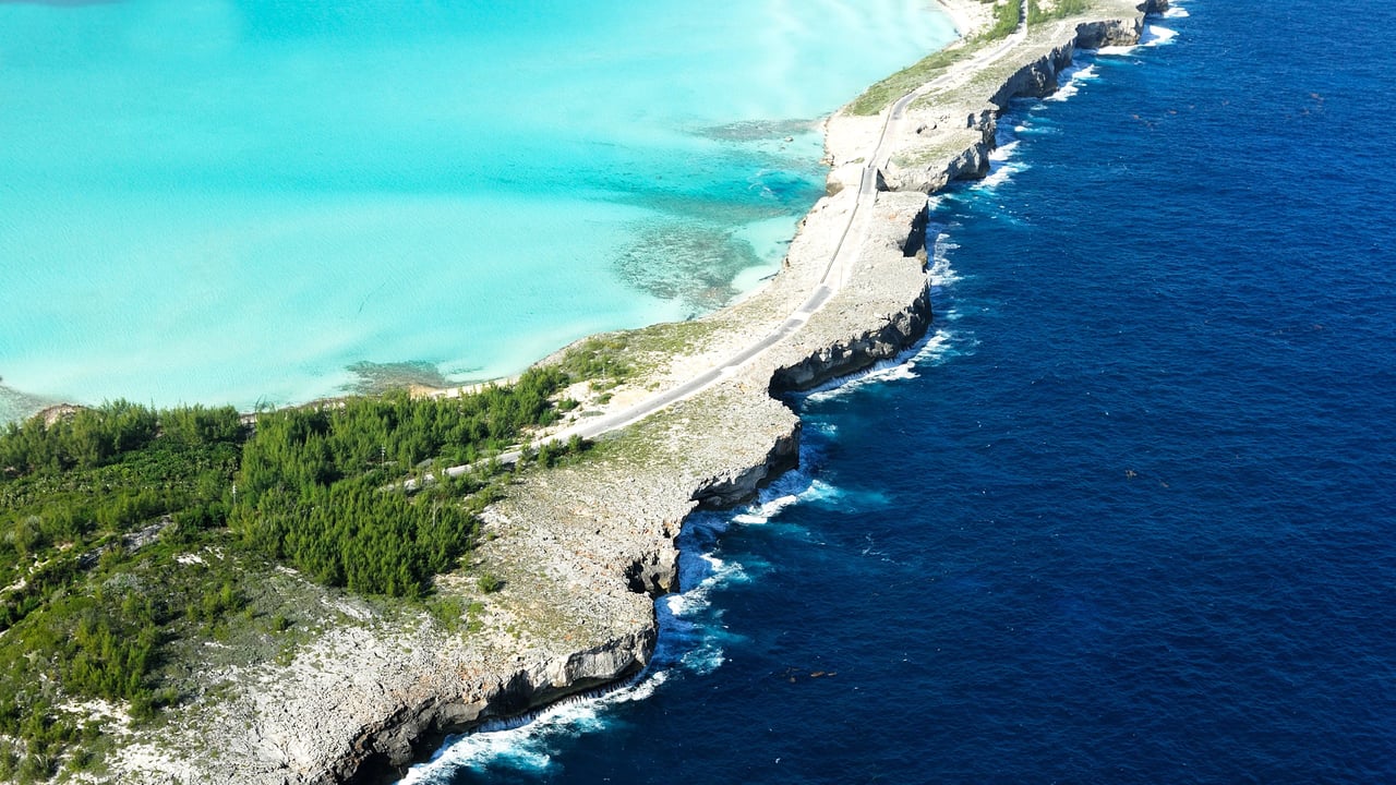 An aerial view of a tropical island coastline with a long, straight road disappearing into the turquoise ocean.