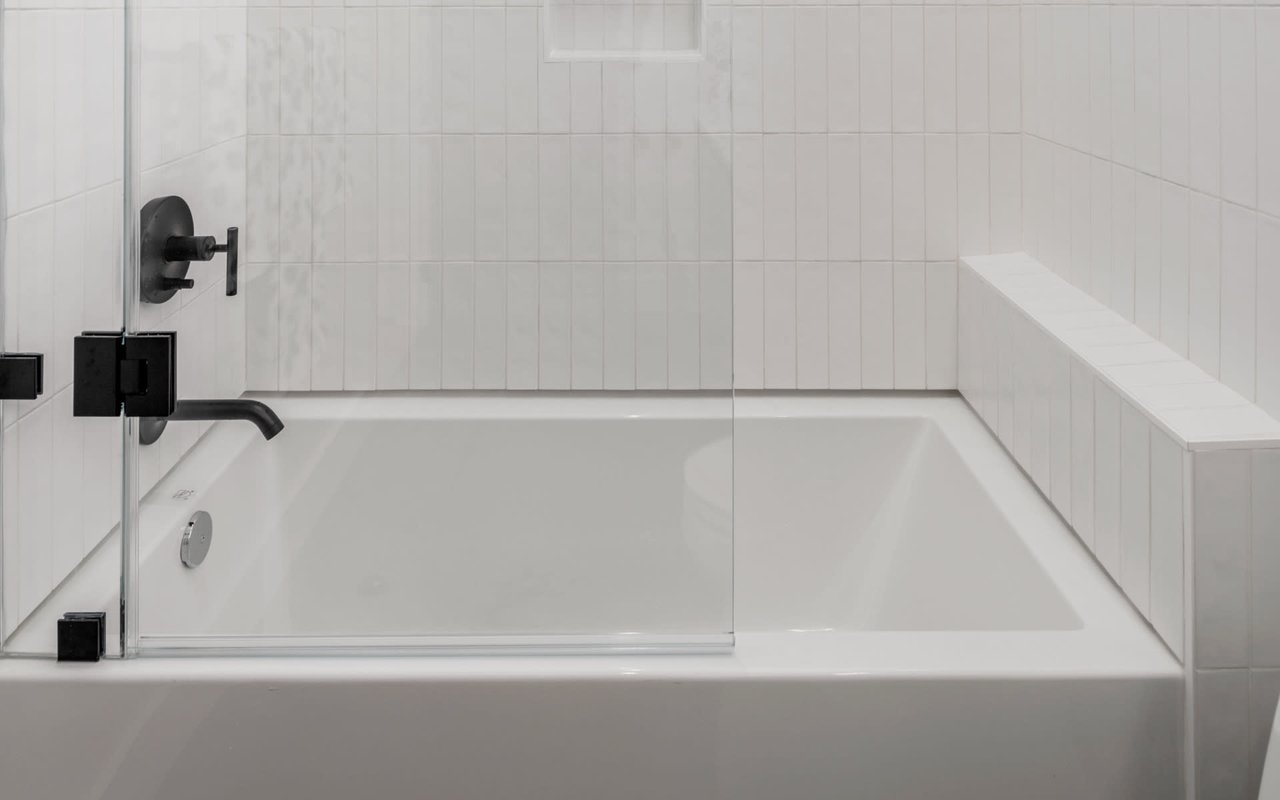 White bathtub with glass shower screen, matte black fixtures, and tiled surround.