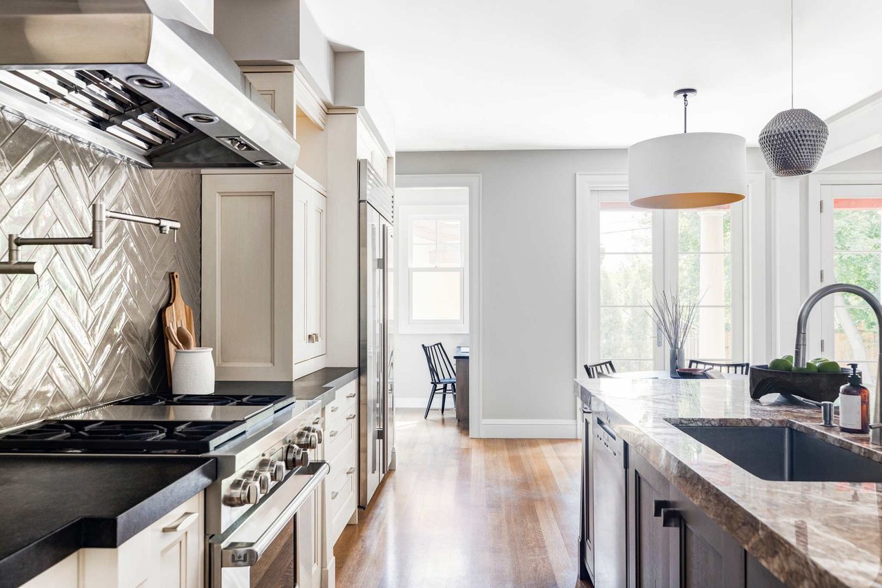 Modern kitchen with chevron backsplash, white cabinets, pro-grade range, and hardwood floors lit by natural light.