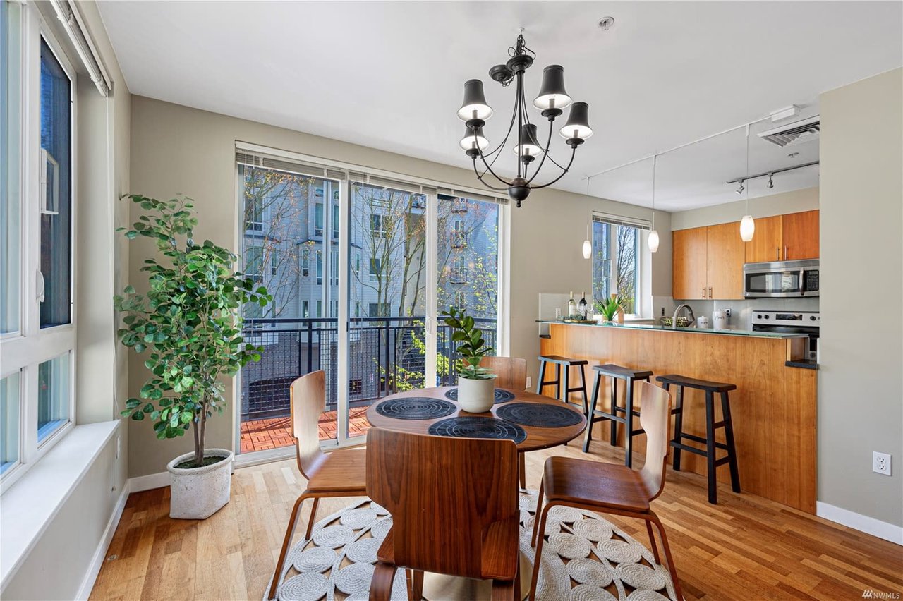 Cozy, well-lit dining space with a modern kitchen, hardwood floors, and balcony views in a chic city condo.