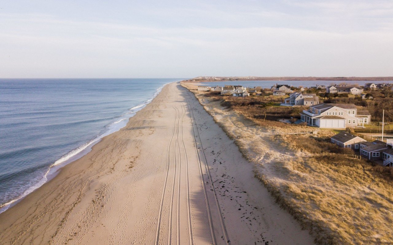 Ariel view of the ocean, sandy beach, and houses in Tom Nevers.