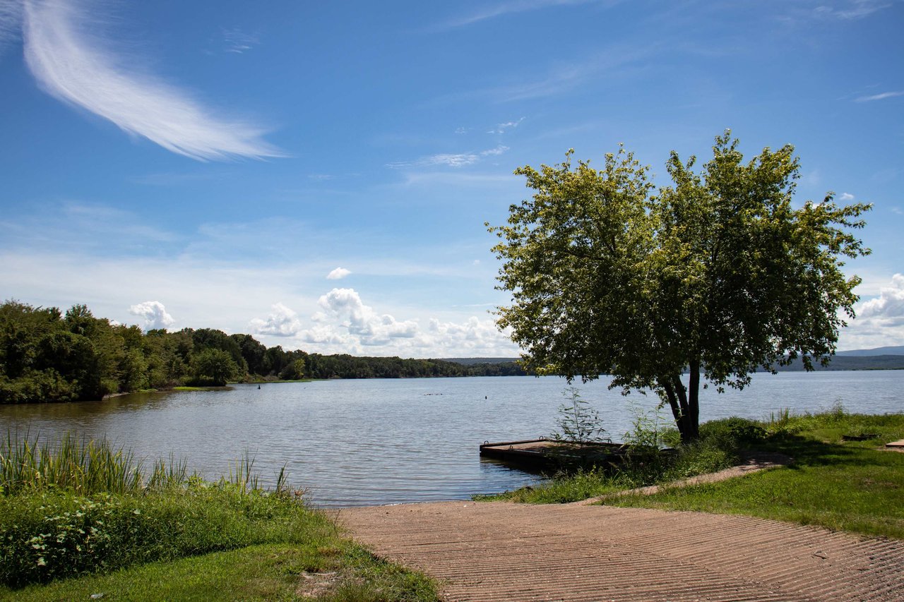 A serene landscape view shows a calm body of water, possibly a lake or a wide river, extending across the midground.