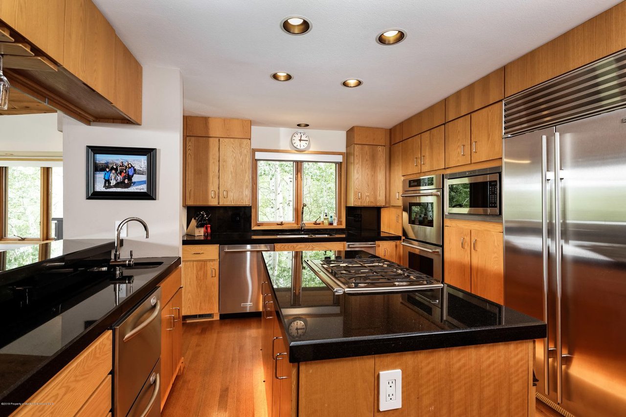 Kitchen with wood cabinetry, black granite counters, stainless steel appliances, and a central cooktop island.