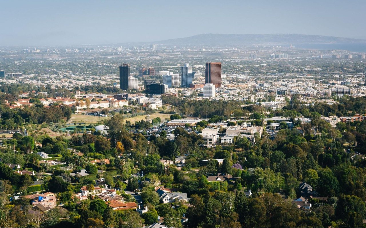 An aerial view of Los Angeles that shows a cityscape with tall buildings, trees, and a road network