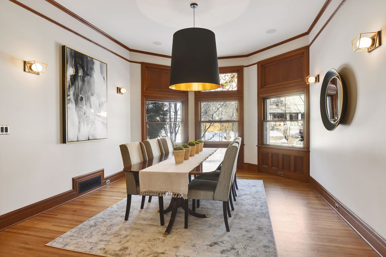 A dining room with a long wooden table and chairs together with a large painting and a mirror at the side.