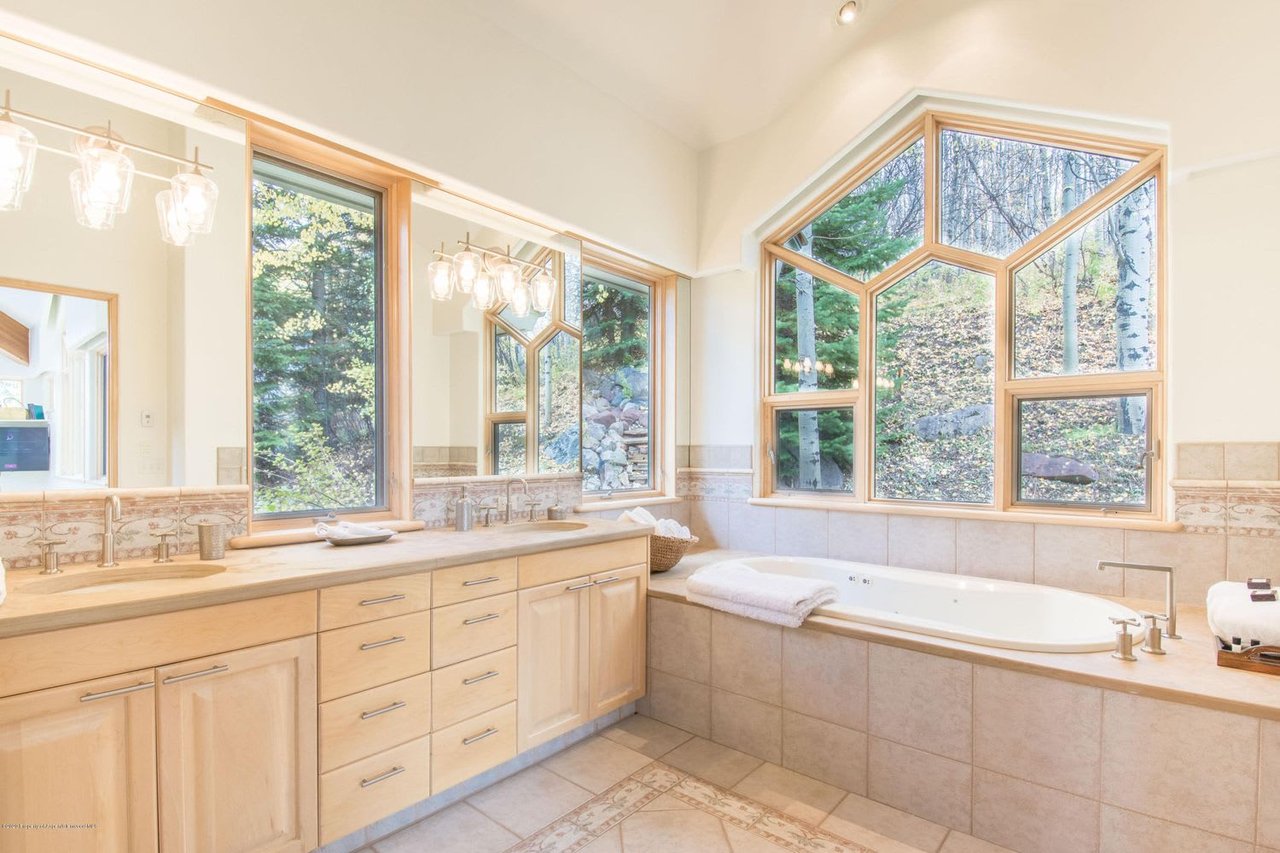 Bathroom with a long wood vanity, soaking tub, and large windows overlooking trees.