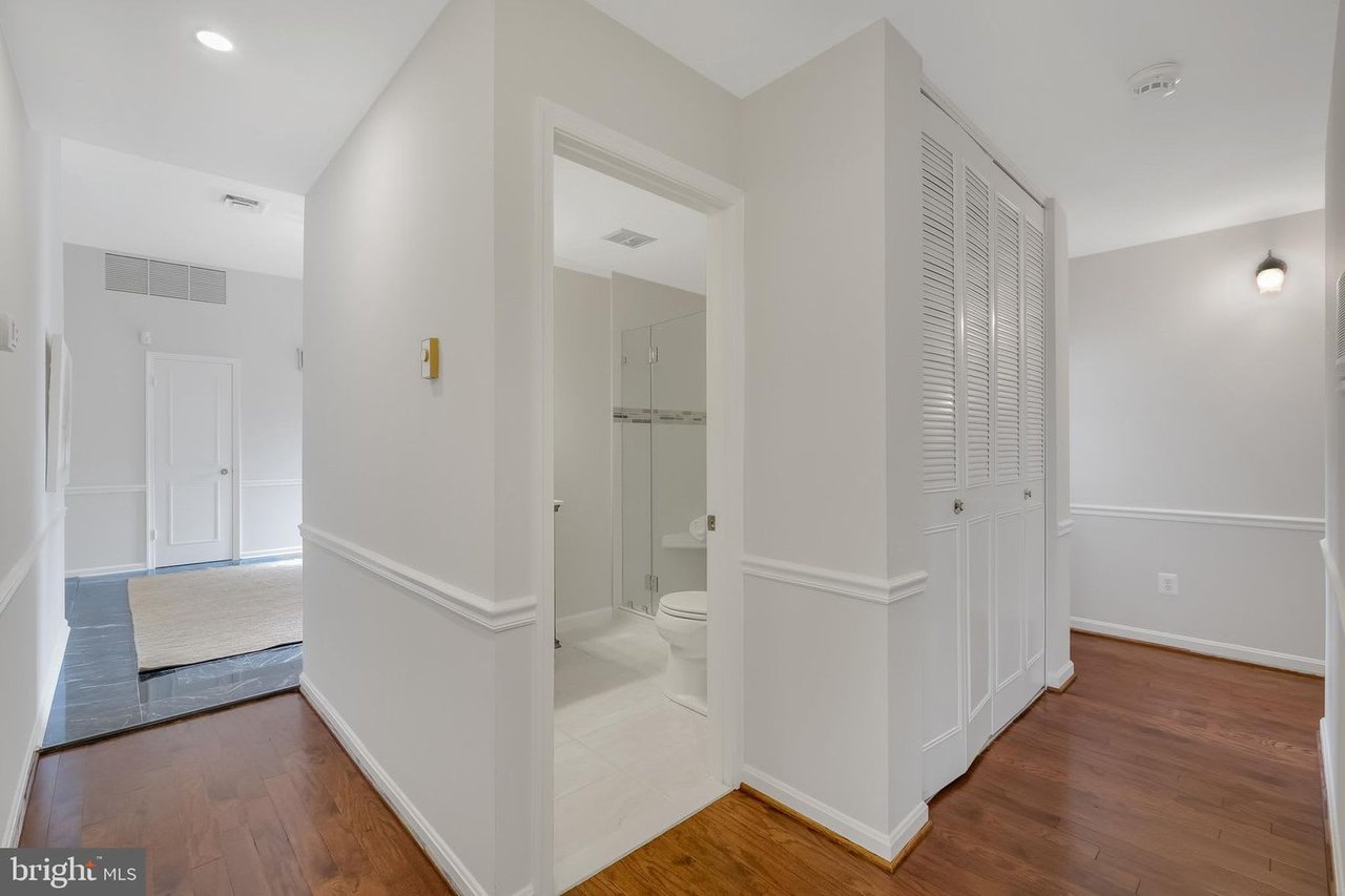 Hallway with hardwood floors, louvered closet doors, and an open bathroom doorway.