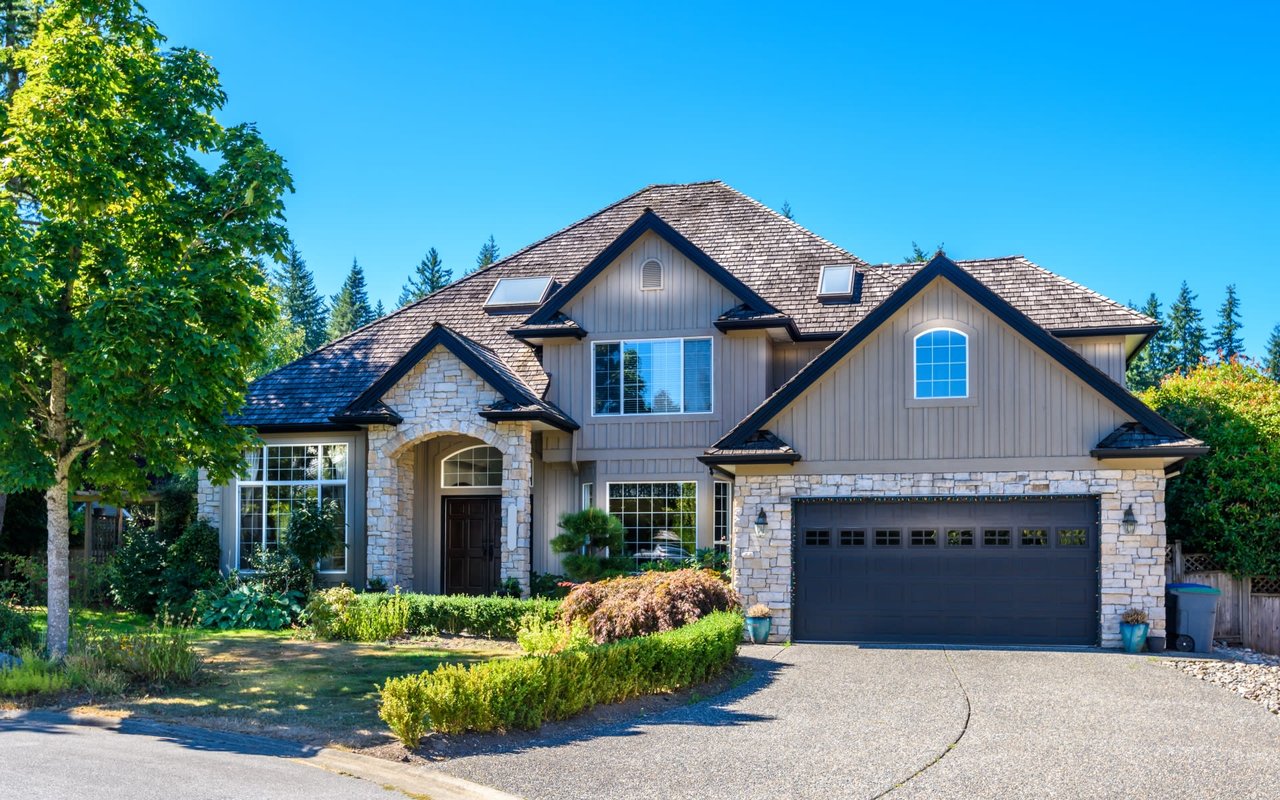 A large house with a black garage door and a driveway in front of it. 