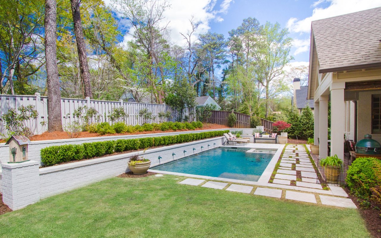 A backyard with a large swimming pool and brick walkway