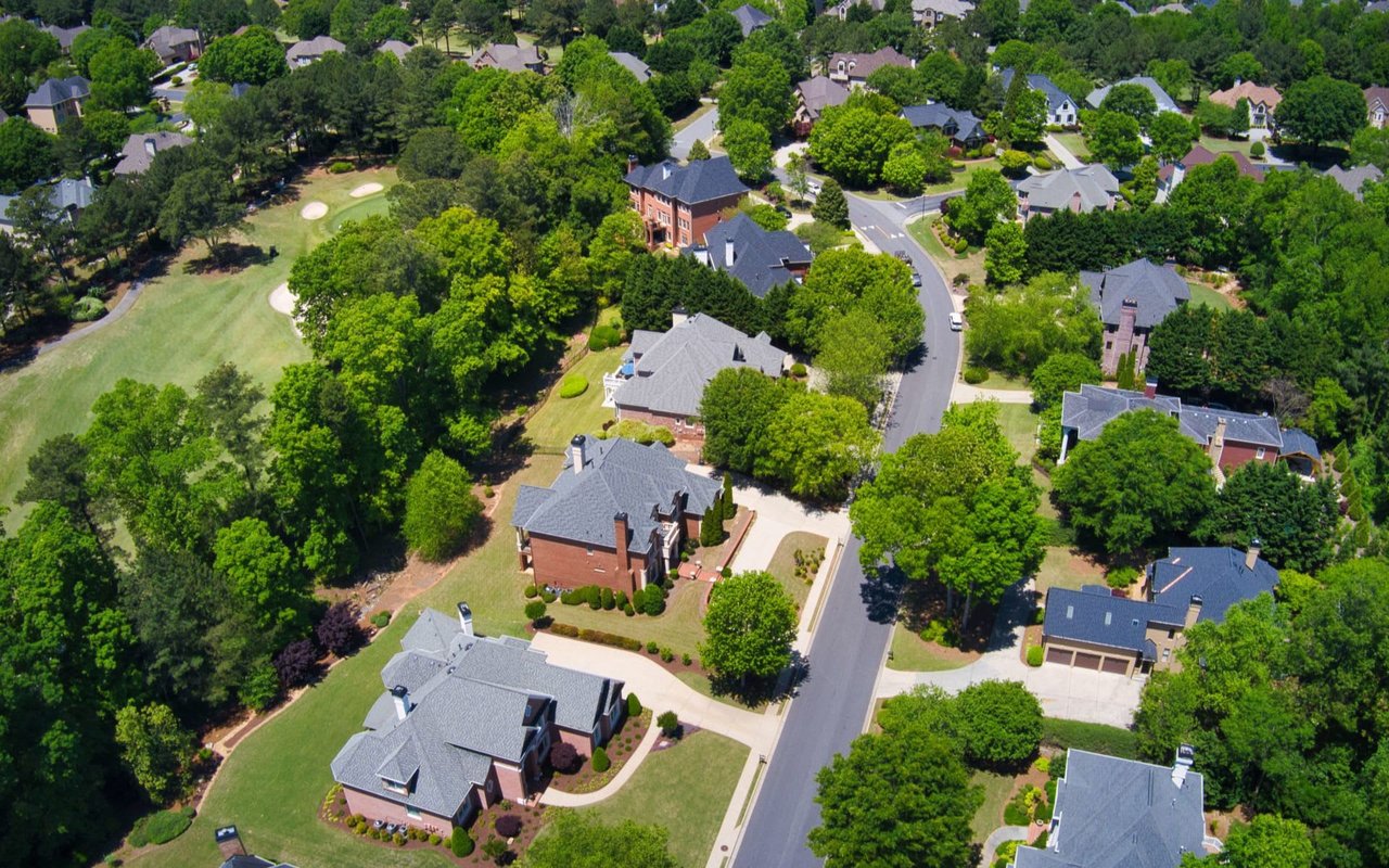 Aerial view of a residential neighborhood with brick homes, tree-lined streets, and a nearby golf course.